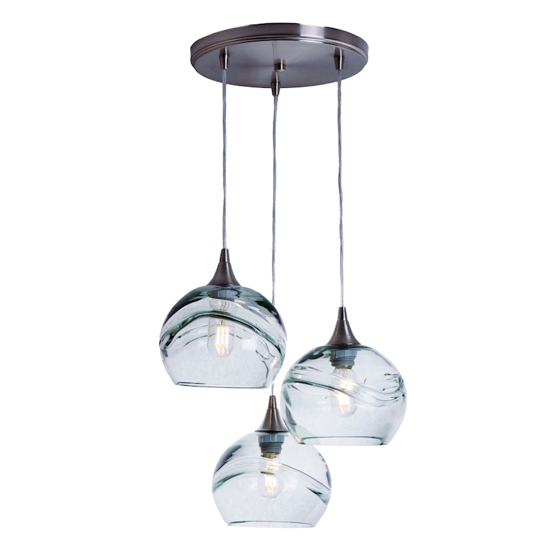 May include: A three-light pendant light fixture with a brushed nickel finish and clear glass shades. The shades have a wavy, textured design.
