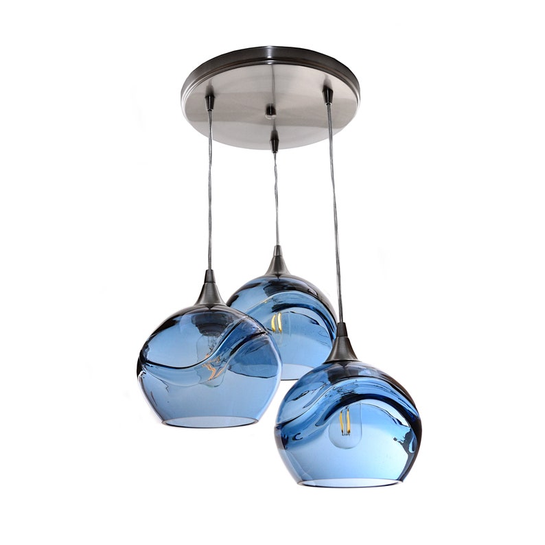 May include: Three blue glass pendant lights with a wave design hang from a silver ceiling plate.