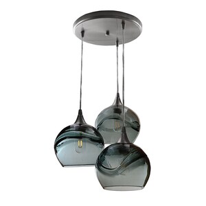 May include: Three gray glass globe pendant lights with a black metal finish and a black metal ceiling plate.