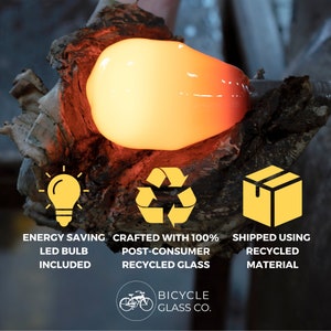May include: A close-up of a glowing orange glass light bulb being made. The image includes three icons: a light bulb, a recycling symbol, and a box. The text below the icons reads: "Energy Saving LED Bulb Included", "Crafted with 100% Post-Consumer Recycled Glass", and "Shipped Using Recycled Material". The text at the bottom of the image reads: "Bicycle Glass Co."