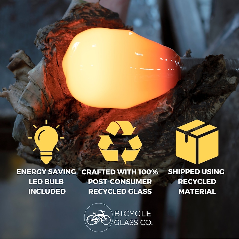 May include: A close-up of a glowing orange glass light bulb being made. The image includes three icons: a light bulb, a recycling symbol, and a box. The text below the icons reads: "Energy Saving LED Bulb Included", "Crafted with 100% Post-Consumer Recycled Glass", and "Shipped Using Recycled Material". The text at the bottom of the image reads: "Bicycle Glass Co."