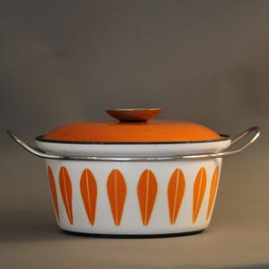 Könnte beinhalten: Eine Vintage-Emaille-Kochtopf in Weiß und Orange. Der Topf hat ein Muster aus orangefarbenen Blattformen und einen silbernen Griff. Der Deckel ist orange mit einem kleinen braunen Knopf. Ein klassischer Küchenartikel.