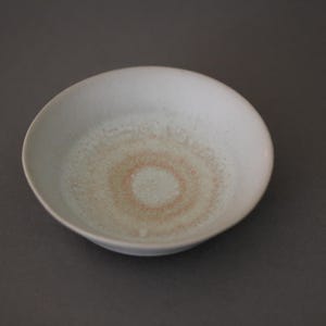May include: A small, white ceramic bowl with a light brown and white concentric circle design in the center.