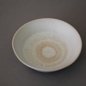 May include: A white ceramic bowl with a light brown, circular pattern in the center.