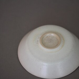May include: A white ceramic bowl with a slightly raised rim and a circular indentation in the center. The bowl has a smooth, glossy finish.