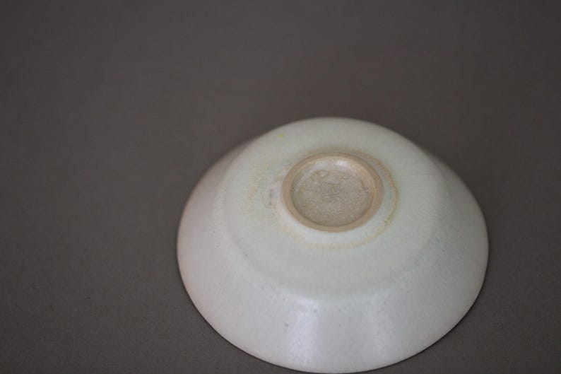 May include: A white ceramic bowl with a slightly raised rim and a circular indentation in the center. The bowl has a smooth, glossy finish.