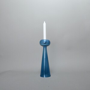 May include: A blue glass candle holder with a white candle. The holder has a round base and a tall, slender stem.