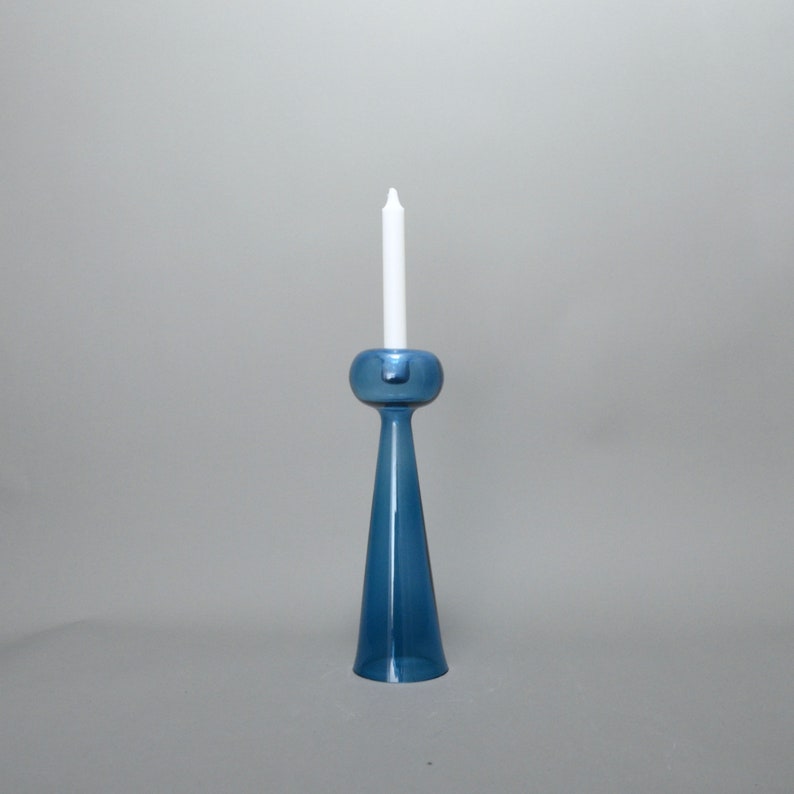 May include: A blue glass candle holder with a white candle. The holder has a round base and a tall, slender stem.