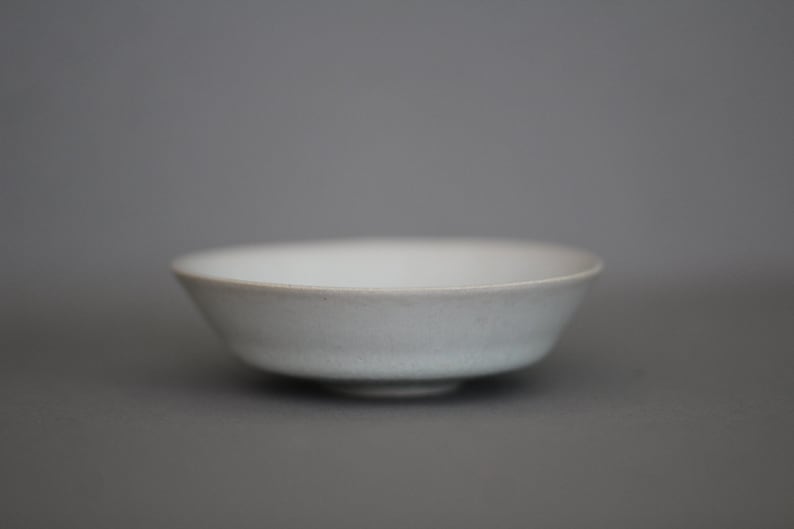 May include: A white ceramic bowl with a slightly rounded bottom and a smooth, glossy finish.