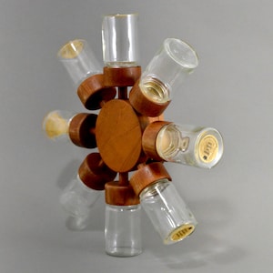 Puede incluir: Un estante de especias de madera con ocho frascos de vidrio. El estante está hecho de madera oscura y tiene una base circular. Los frascos son de vidrio transparente y tienen tapas de metal.