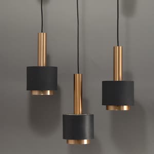 Könnte beinhalten: Drei Pendelleuchten mit modernem Design. Jede Leuchte hat einen zylindrischen, schwarzen Schirm, einen goldfarbenen Metallsockel und einen goldfarbenen Metallschaft. Die Leuchten hängen an schwarzen Kabeln vor grauem Hintergrund.