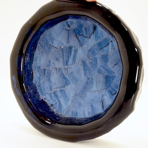 May include: A round, blue ceramic dish with a black rim. The dish has a textured surface and a glossy finish.