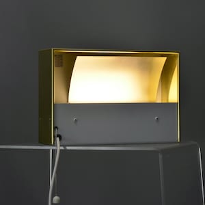 May include: A gold-colored wall sconce with a white interior and a frosted glass diffuser. The sconce has a cord with a pull chain switch.