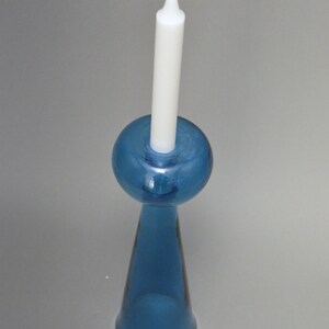 May include: A blue glass candle holder with a round top and a conical base. A white candle is placed in the holder.