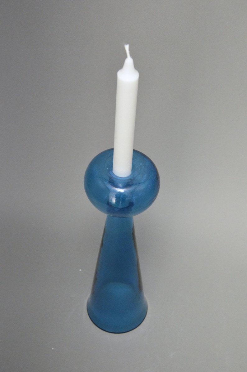 May include: A blue glass candle holder with a round top and a conical base. A white candle is placed in the holder.