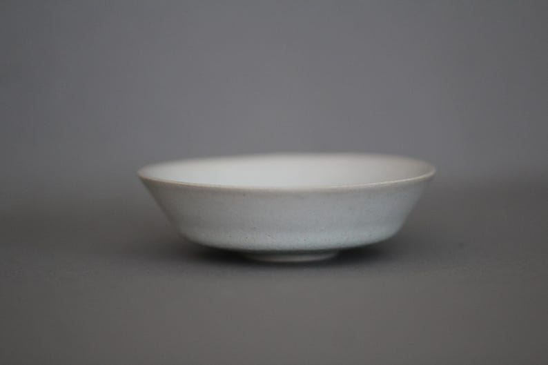 May include: A white ceramic bowl with a slightly textured surface. The bowl is shallow and has a rounded shape.