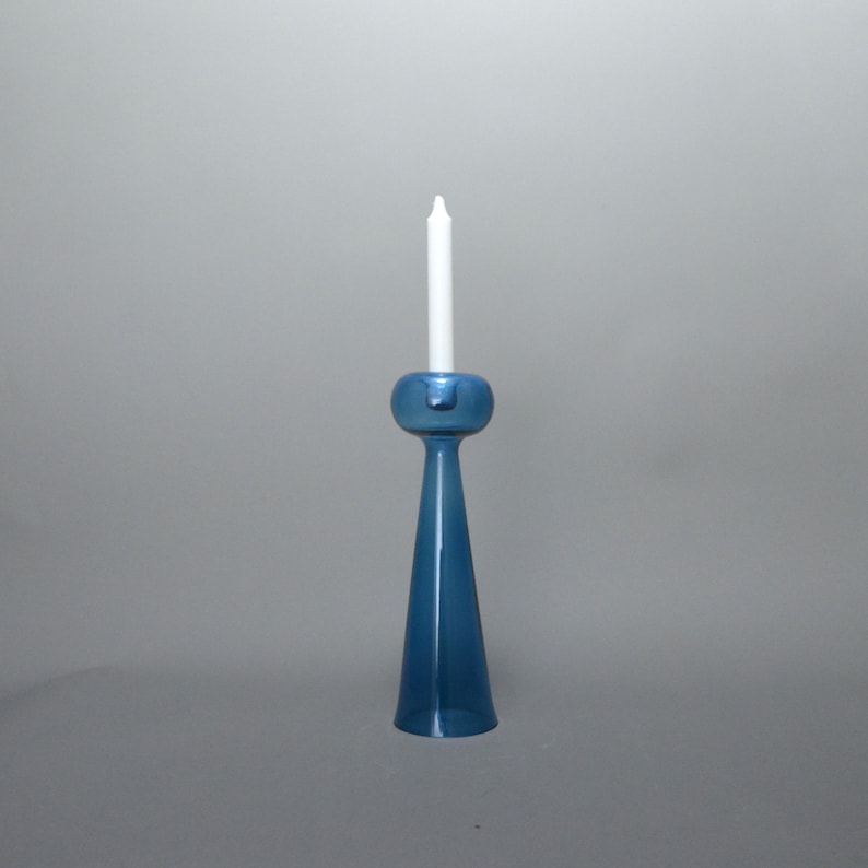 May include: A blue glass candle holder with a round top and a tall, tapered base. A white candle is placed in the holder.