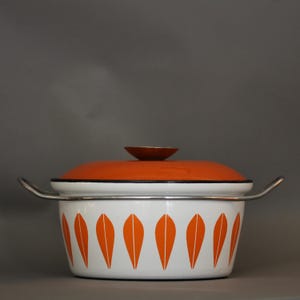 Könnte beinhalten: Ein Vintage-Topf aus Emaille mit weißem Korpus und orangefarbenem Blattmuster. Der Topf hat einen orangefarbenen Deckel mit einem kleinen braunen Knauf und silbernen Griffen. Der Rand des Topfes und des Deckels ist schwarz.