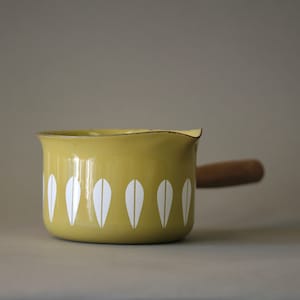 Op de afbeelding: Een gele emaille steelpan met een houten handvat. De pan heeft een wit druppelpatroon rond de basis. De rand heeft een gouden rand. Deze vintage-stijl steelpan is ideaal om in te koken.