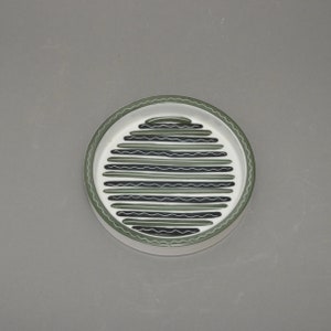 May include: A white ceramic dish with a green and black geometric pattern. The pattern is made up of horizontal lines and wavy lines.