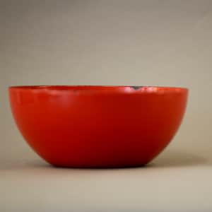 Puede incluir: Un cuenco de cerámica naranja brillante con un borde negro. El cuenco está vacío y se encuentra sobre una superficie blanca.