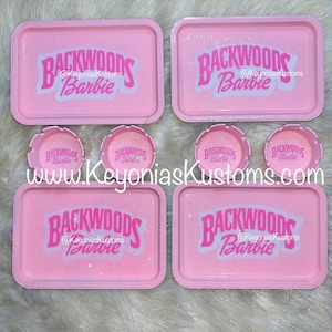 Pode incluir: Bandejas e cinzeiros cor-de-rosa com as palavras "Backwoods Barbie" e o texto "@KeyoniasKustoms".