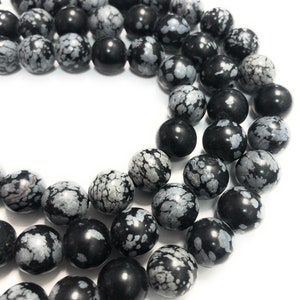 May include: A strand of black and white snowflake obsidian beads. The beads are round and have a speckled pattern.
