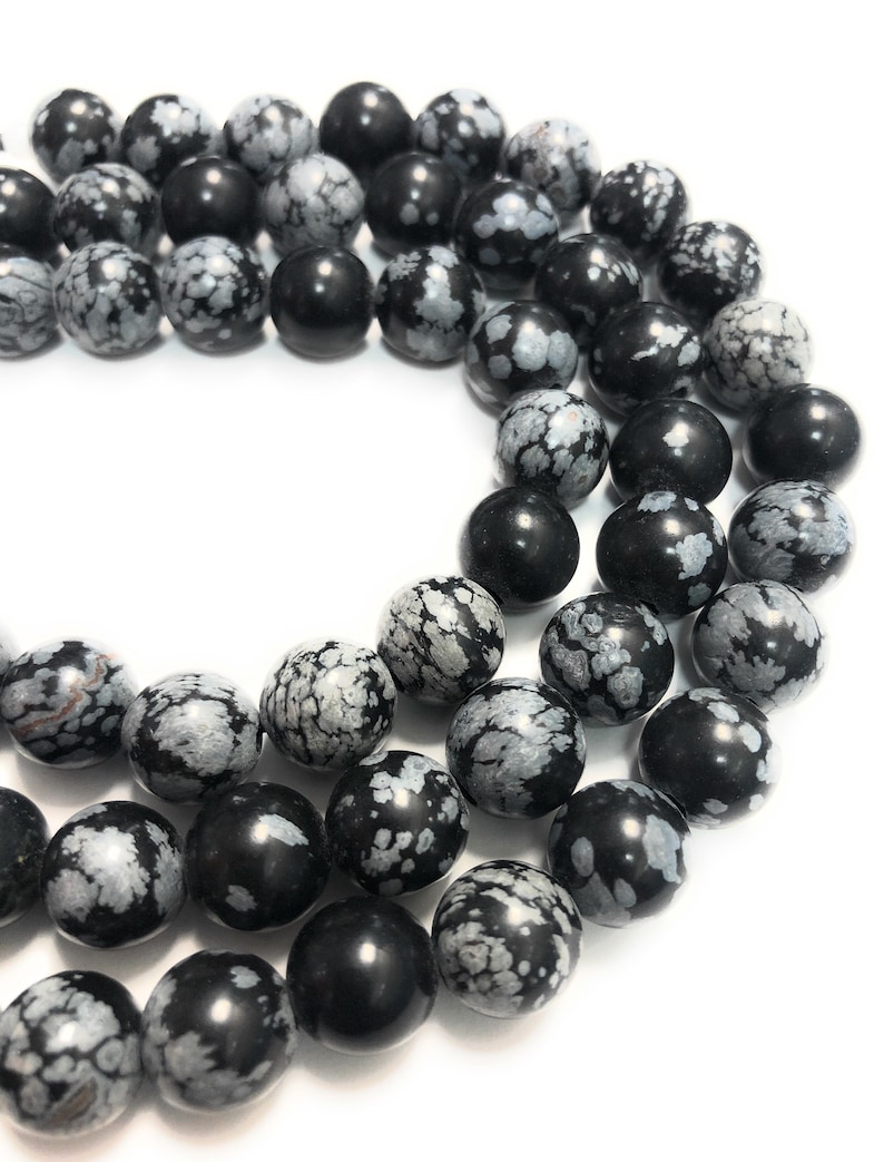 May include: A strand of black and white snowflake obsidian beads. The beads are round and have a speckled pattern.