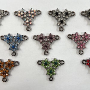 May include: Ten different colored metal charms with three flower designs each, featuring rhinestones. The charms have a loop on the bottom for attaching to jewelry.