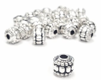May include: A pile of silver metal beads with a textured design. The beads are round and have a hole in the center.