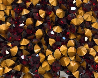 May include: A close-up image of a pile of red and gold rhinestones. The rhinestones are small and round, with a flat back and a pointed top. They are arranged in a random pattern, with some of the rhinestones overlapping.