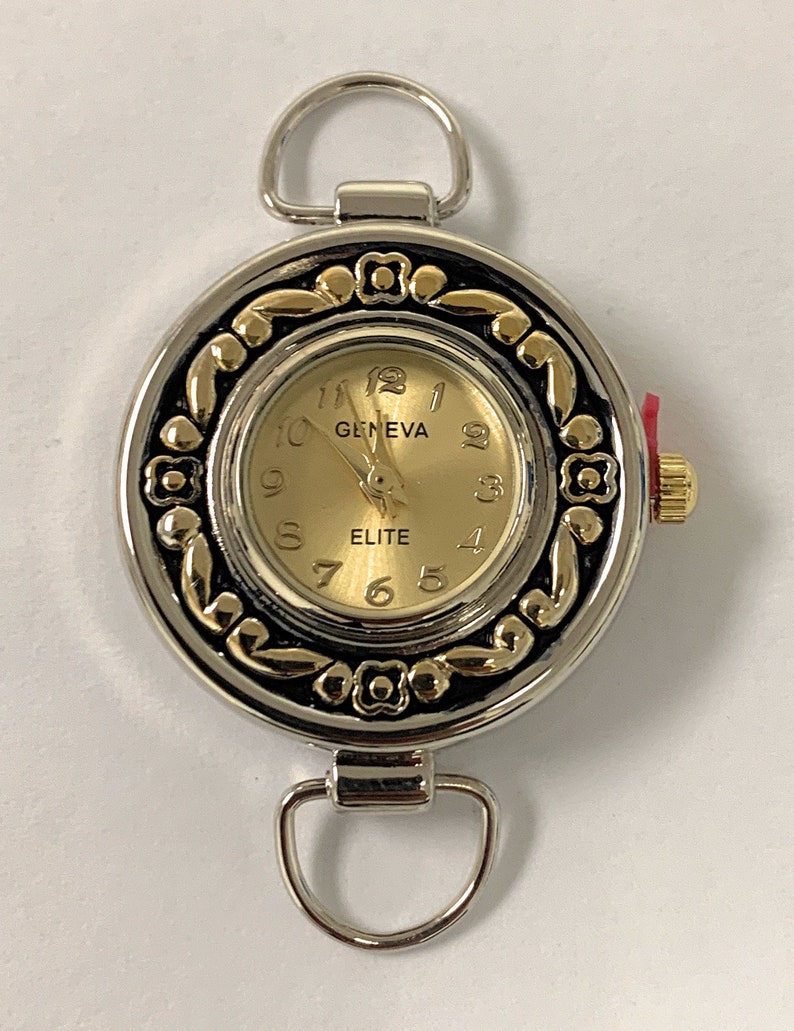 May include: A silver and gold tone watch with a round face and a black and gold patterned border. The watch face is gold with black numbers and the words "GENEVA" and "ELITE".