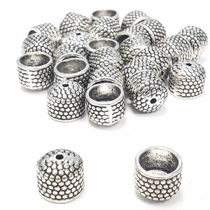 May include: A pile of silver metal bead caps with a textured surface. The caps are round with a hole in the center.