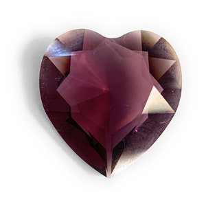 May include: A heart-shaped, faceted gemstone with a deep purple hue. The gem is cut with a star-shaped pattern and has a high polish.