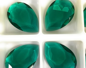 May include: Four pear-shaped green glass gems in a white plastic tray. The gems are faceted and have a clear, shiny finish.