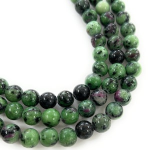 May include: A strand of green, black, and pink gemstone beads. The beads are round and have a speckled appearance.