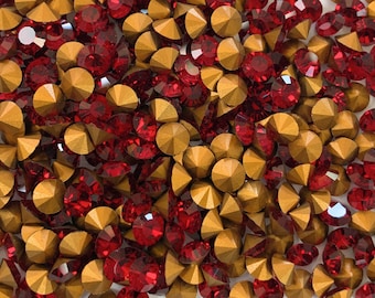 May include: A close-up image of a pile of red and gold rhinestones. The rhinestones are small and round, with a pointed back.
