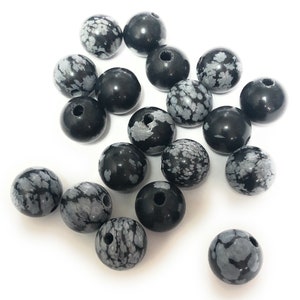 May include: A collection of 17 black and white speckled round beads. The beads are made of snowflake obsidian.