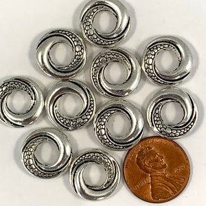 May include: Ten silver-toned metal rings with a swirl design and a textured surface. The rings are approximately the size of a US penny.