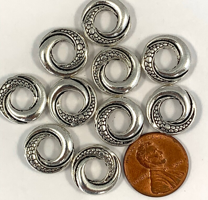 May include: Ten silver-toned metal rings with a swirl design and a textured surface. The rings are approximately the size of a US penny.