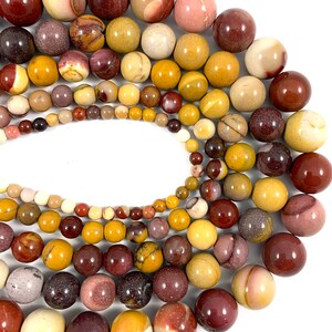 May include: A collection of round, polished gemstone beads in shades of brown, red, and yellow. The beads are arranged in a circular pattern, with the largest beads in the center and the smallest beads on the outside.