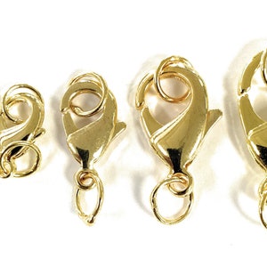 May include: Five gold-colored lobster claw clasps of varying sizes are arranged in a row. Each clasp has a spring-loaded mechanism and a small loop for attaching to jewelry or other items. The clasps are on a white background.