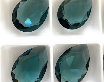 May include: Four teardrop-shaped, faceted, teal blue glass gems in a white display tray.