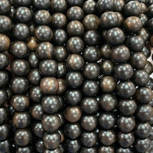 May include: A close-up of a pile of black wooden beads. The beads are round and smooth, and they have a slightly shiny finish.