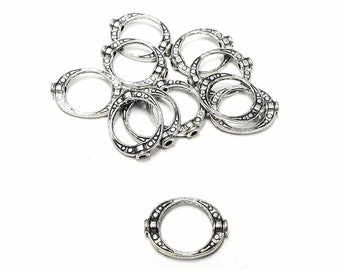 May include: A group of ten silver-toned metal rings with a decorative design. The rings are about 1 inch in diameter and have a slightly rounded shape.