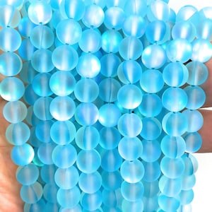 May include: A strand of light blue frosted glass beads. The beads are round and have a smooth, matte finish.