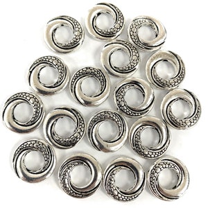 May include: A collection of 15 silver-toned metal beads with a swirl design. Each bead has a circular shape with a hole in the center. The beads are perfect for jewelry making or crafting.