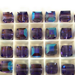 May include: A close-up view of a white plastic container filled with 20 iridescent purple square beads. The beads are arranged in a grid pattern.