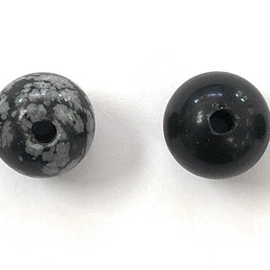 May include: Four round black and white speckled beads with a hole through the center.
