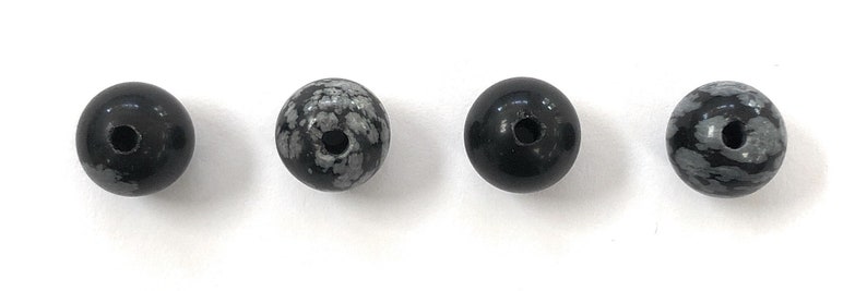 May include: Four round black and white speckled beads with a hole through the center.